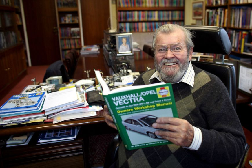 A man sitting in a library, in a chair holding a book